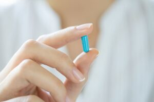 Woman holding blue capsule of biotin