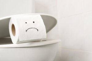 sad face on toilet paper wedged onto a toilet seat